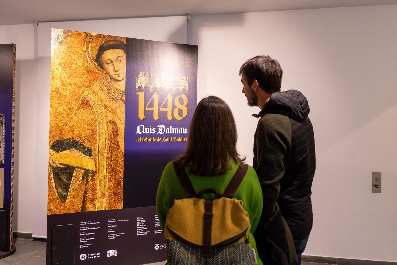 Dos personas, mirando el cartel de la exposición en la entrada.